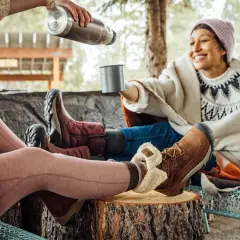 Cozy friends share drinks outdoors, their feet snug in warm shoes to keep feet warm.
