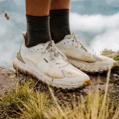 A pair of well-worn, white norda 001a trail running shoes stand on a rocky, grassy peak, ready for adventure.