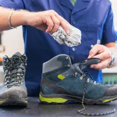 A person stuffs crumpled paper into a hiking boot, demonstrating the best way to dry boots after a muddy adventure.