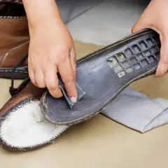 Hands gently sanding the sole of a brown leather boot, demonstrating how to clean Vibram shoes for better grip.