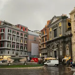 Rainy day in Naples, with colorful buildings, a fountain, and parked scooters. A perfect scene for a 2 days in Naples adventure.