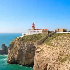 Lighthouse on a cliff overlooking the ocean, part of the fisherman's trail Portugal. Rugged coastline with a stone wall leading to the fort.