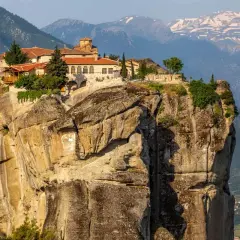 Monastery perched atop a massive rock formation in Meteora, Greece. The ancient stone buildings with red-tiled roofs seem to defy gravity, offering a glimpse into timeless Meteora hours.