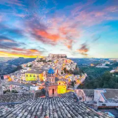 A picturesque Italian town perched on a hill, bathed in the warm glow of sunset. This view captures the essence of **two weeks in Sicily**, with its charming architecture and vibrant sky.