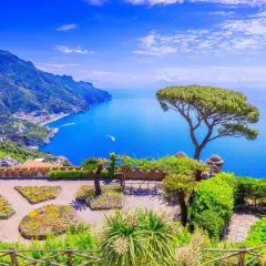 A stunning view of the Amalfi Coast, a perfect destination for a trip from Naples. Lush gardens overlook the sparkling blue sea and dramatic cliffs.
