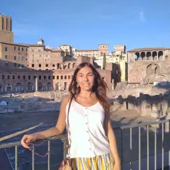 A woman smiles in front of ancient Roman ruins, enjoying a sunny day. This scene suggests that Rome is safe and welcoming for tourists.
