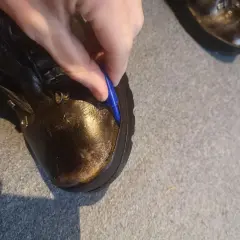A hand uses a blue tool to pry open a seam on a leather boot, showing how to fix boots that are coming apart.