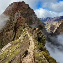 A stone path winds along a narrow mountain ridge, offering what is likely the best hiking in Portugal. Clouds drift through the dramatic, rugged peaks.