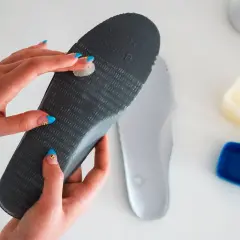 Hands with blue nails apply balm to an insole, solving why are my tennis shoes squeaking.