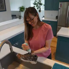 A woman cleans a dirty boot in a kitchen sink, preparing it for the washer.