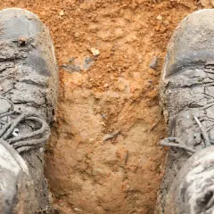 Mud-caked boots stand in dirt. The question "do boots shrink over time?" lingers as these boots look like they've seen many adventures.
