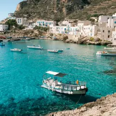 A picturesque harbor with white buildings and boats, showcasing one of the top places to see in Sicily.
