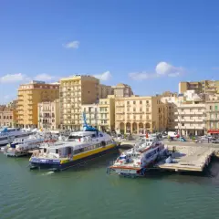 Ferries docked in a harbor, with buildings lining the waterfront. Wondering if you can drive to Sicily? These ferries might be your answer!