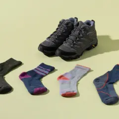 Hiking boots and six pairs of colorful socks are laid out. Is wearing two pairs of socks bad? This image shows options for comfort.