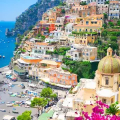 Colorful towns near Naples, Italy, cascade down a cliff to a busy beach and blue sea. A domed church stands out.