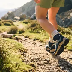 Hiking boots, one leather, one synthetic, tread a rocky path through a sun-drenched mountain landscape.