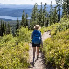 A hiker with a blue backpack walks on a trail, enjoying one of the best long hikes in the world with a stunning lake and mountain view.
