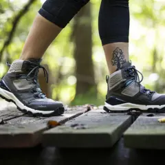 A person walks on a wooden path in the forest, wearing hiking boots. One foot half size bigger than the other, with a tree tattoo on the ankle.