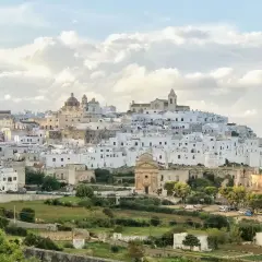 A white city perched on a hill, reminiscent of a scene from Puglia, Italy, with a church and scattered buildings.