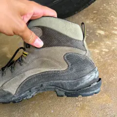 A hand holds a worn hiking boot, showing why shoe soles crack: exposure to elements and heavy use can cause the rubber to degrade and split.