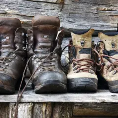 Four pairs of hiking boots, two dark brown leather and two tan, sit on a wooden shelf. Considering if you should size up in hiking shoes?