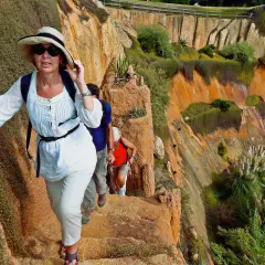 Hikers ascend a rocky path during hiking trips in Portugal, with lush green vegetation clinging to the orange cliffs.