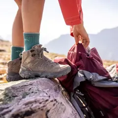 A hiker prepares for the trail, choosing between low vs mid hiking shoes. Their mid-cut boot offers ankle support on rocky terrain.