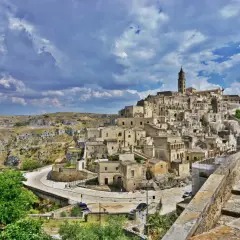 A woman in a patterned dress surveys the ancient Sassi di Matera, Italy. This view offers a glimpse of what to do in Matera Italy: explore its unique cave dwellings and historic architecture.