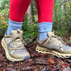 These tan hiking shoes with grey socks and red leggings are perfect for exploring a forest floor covered in pinecones.