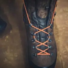 Close-up of a brown hiking boot with bright orange laces tied in a parallel lacing pattern, ready for adventure.