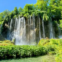 A stunning waterfall cascades down a rocky cliff, surrounded by lush green foliage. Perfect for Croatia hiking trips, this scene captures the natural beauty of Plitvice Lakes National Park.
