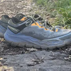 A pair of Merrell Nova 4 trail running shoes rests on a rocky path, ready for adventure.