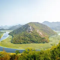 A winding river snakes through lush green hills and a vast wetland, a perfect scene for planning how many days in Montenegro.