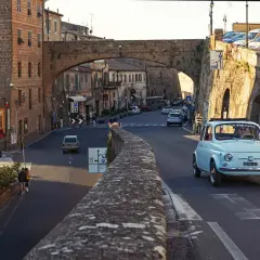 A light blue Fiat 500 drives through a Tuscan town. Do you need a car in Florence to explore charming streets like this?