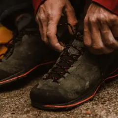 Hands tying red-laced hiking boots. Proper fit is crucial for comfort and performance on the trail.