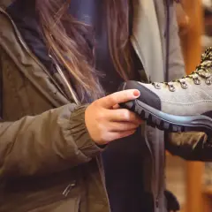 A person in a green jacket holds a hiking boot, considering if boots should fit snug or loose for comfort on the trail.