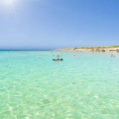 Crystal clear turquoise waters and a sandy beach with sunbathers, perfect for those wondering where to stay in Puglia for beaches.