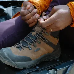 Close-up of hands tying brown hiking boots, demonstrating how to tie hiking boots for an outdoor adventure.