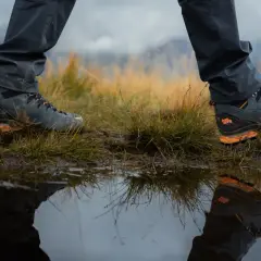 Hiking boots reflected in a puddle. Learn how to get your shoes to stop squeaking on your next adventure.