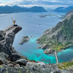 A hiker celebrates on a cliff overlooking turquoise waters and rugged mountains, showcasing some of the best islands for hiking.