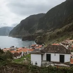 Coastal village with red-tiled roofs nestled against lush green mountains. A perfect place to stay in Madeira, offering stunning ocean views.