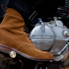 A suede boot rests on a motorcycle engine, ready for a ride. Learn how to walk in boots like these for style and comfort.