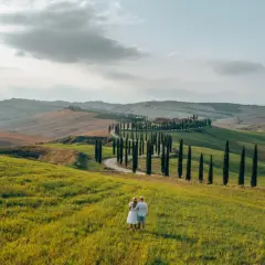 A couple enjoys the view of rolling hills and a cypress-lined road, perfect for renting a car in Tuscany.