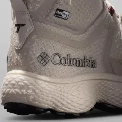 Close-up of a beige Columbia hiking boot with water droplets. The boot features the Columbia logo and "OutDry WATERPROOF" branding, showcasing its durable, water-resistant design.