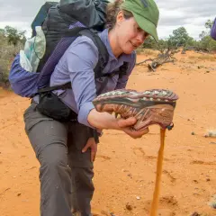 A hiker shakes sand from a shoe, demonstrating the challenge of finding the best shoes for hiking in sand.