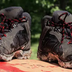 Mud-caked hiking boots with red and black laces sit on a red surface. These boots show signs of heavy use, hinting at how long do hiking boots last.