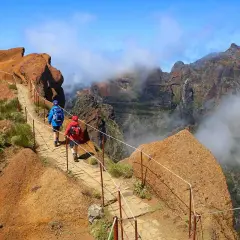 Hikers on a mountain path, a perfect example of things to do in Madeira. Dramatic cliffs and clouds surround them.