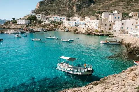 A picturesque harbor with white buildings and boats, showcasing one of the top places to see in Sicily.