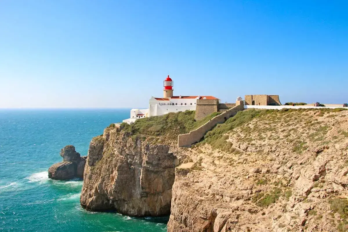 Lighthouse on a cliff overlooking the ocean, part of the fisherman's trail Portugal. Rugged coastline with a stone wall leading to the fort.