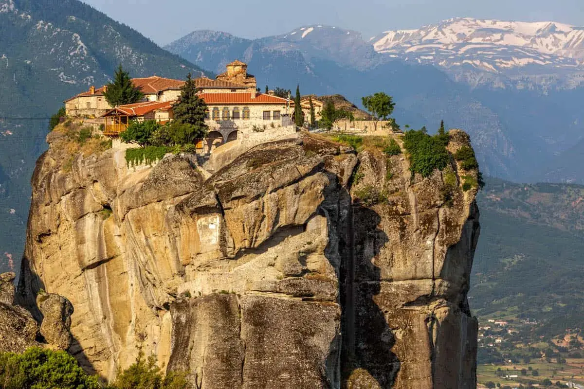 Monastery perched atop a massive rock formation in Meteora, Greece. The ancient stone buildings with red-tiled roofs seem to defy gravity, offering a glimpse into timeless Meteora hours.